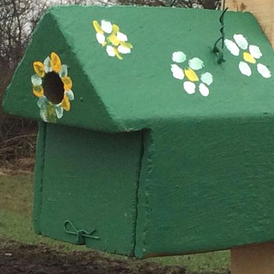 bunt gestalteter Nistkasten hängt an der neu gepflanzten Hecke